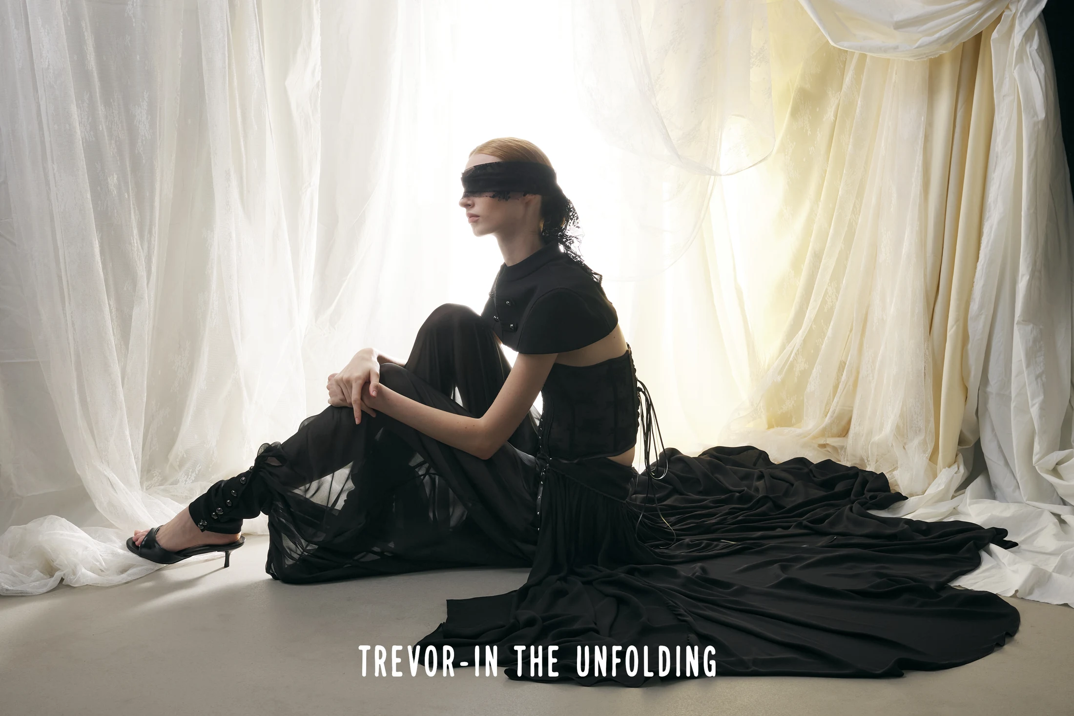 Black corseted silhouette and flowing sheer layers against draped ivory fabric